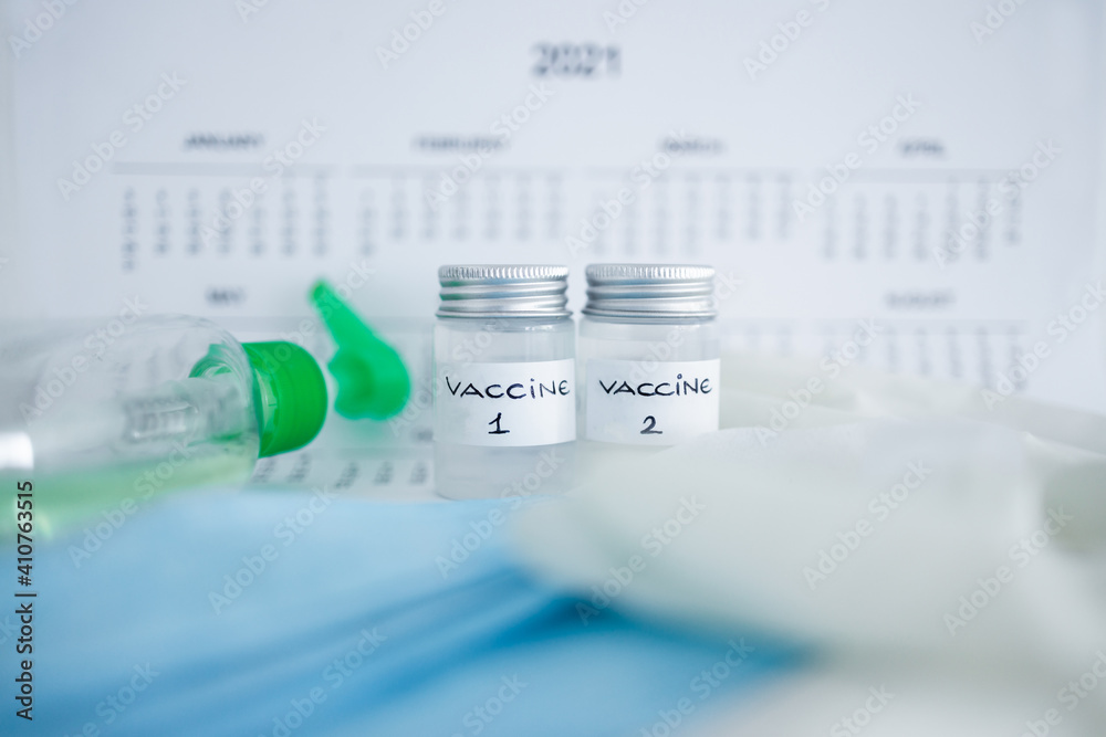 covid-19 vaccine against the pandemic, ampoules with Vaccine 1 and Vaccine 2 labels side by side next to 2021 yearly calendar and mask gloves and sanitizer