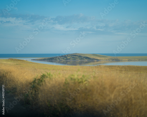 Fototapeta Naklejka Na Ścianę i Meble -  
A beautiful deserted view of the field, tall grass, reflection of the hill in the lake bay.