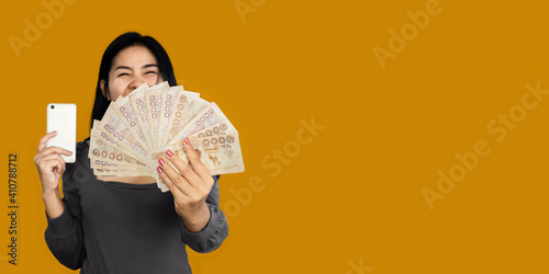 Canvas-taulu happy Asian woman showing Thai baht money another hand holding smart phone over
