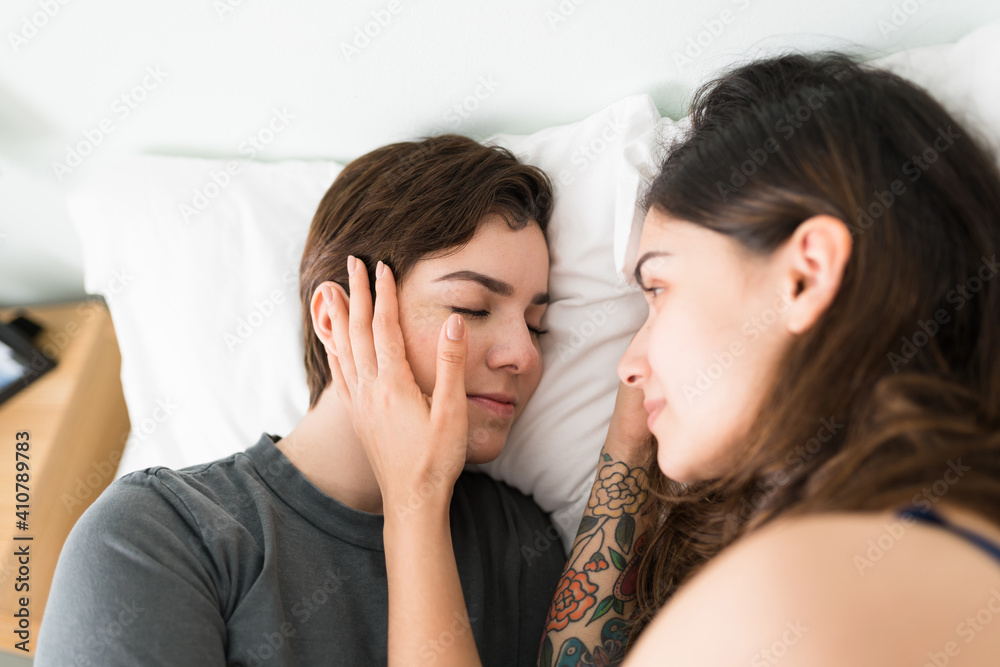 Hispanic woman watching his girlfriend sleeping in their bed Hispanic woman watching his girlfriend sleeping in their bed