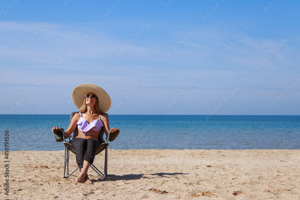 journey to the sea. girl in a bathing suit and hat sunbathing on the beach. tourist sitting on the sand. leisure wear. copy space