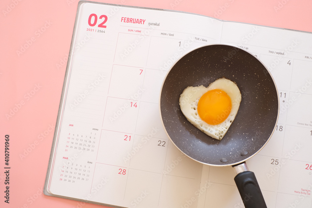 Heart shape fried egg in the pan on the calendar isolated on pink background. top view. Valentine's day concept. Copy space for text Heart shape fried egg in the pan on the calendar isolated on pink background. top view. Valentine's day concept. Copy space for text