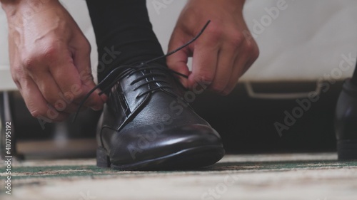 The man is tying the shnzrki on black shoes. Putting on men's shoes in the morning before going to work. Hands close-up