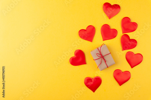 Gift box with ribbon and red hearts on yellow colored background, valentine's day greeting card