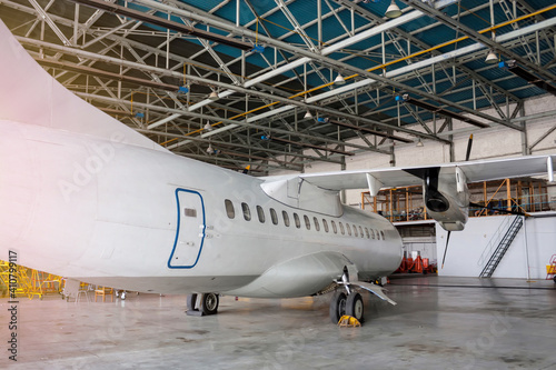 White passenger turboprop aircraft under maintenance in the hangar. Repair of airplane and checking mechanical systems for flight operations