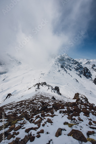 View of mountain peaks and rocks covered with snow around the clouds under the blue sky