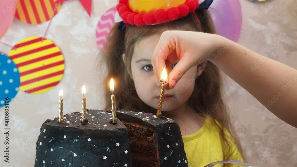 Portrait of little pretty girl with birthday cake a girl in a cap celebrates her birthday, has fun, blows a pipe, blows out the candles on the cake, eats a cake, drinks juice, wears a mask 