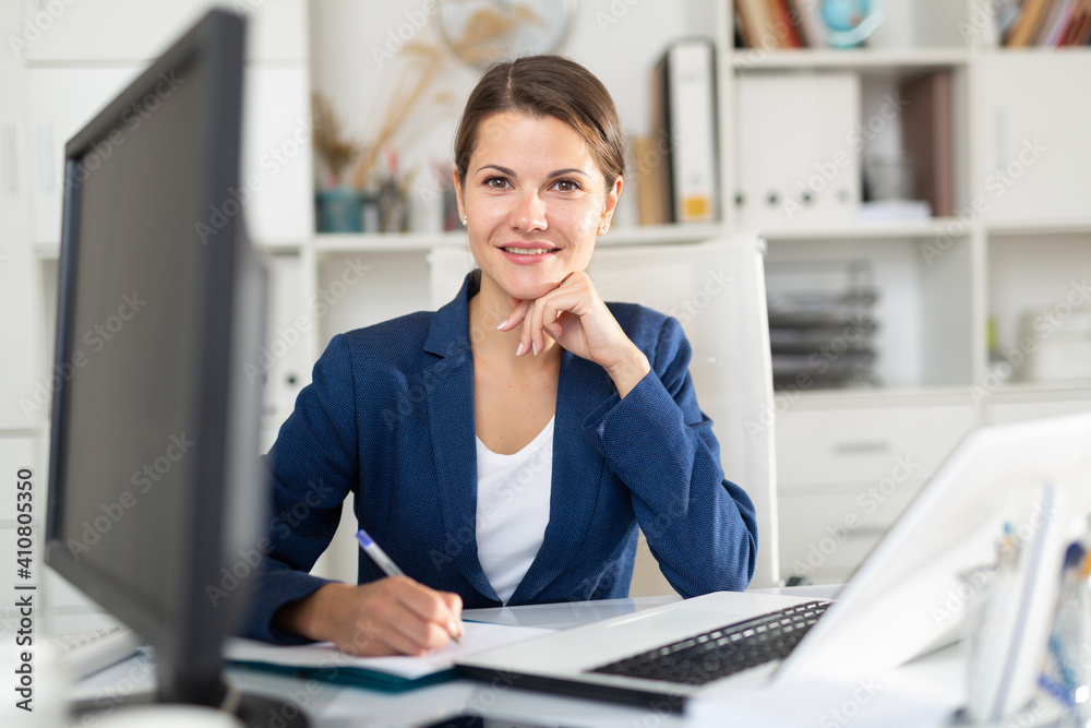 Portrait of successful busy female entrepreneur sitting at office desk with papers and laptop - obrazy, fototapety, plakaty 