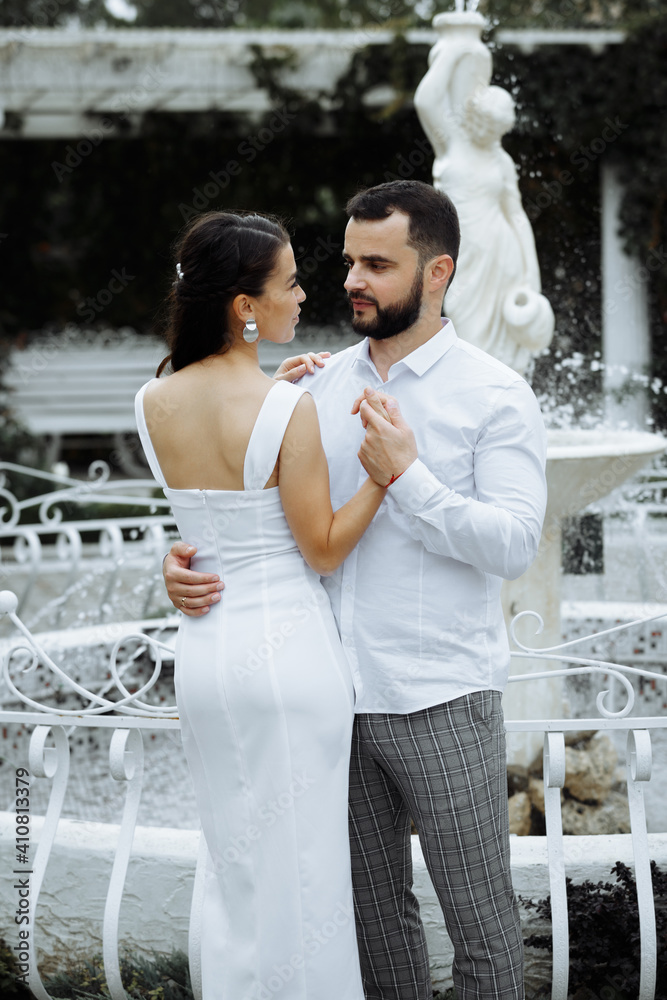Naklejka premium Stylish couple gently hugging on the background of the fountain. Happy sensual wedding couple embracing. Romantic moments of newlyweds.