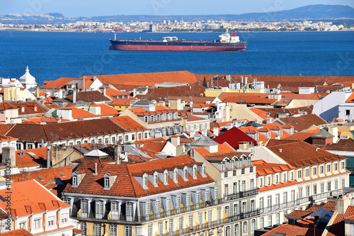 Red roofs of Lisbon against the background of a cargo ship sailing on the Tagus River. Lisbon, Portugal