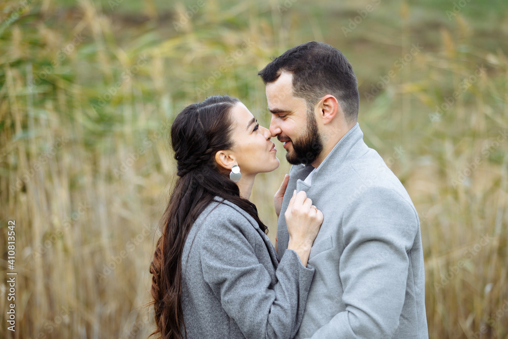 Stylish couple in gray coats gently hugging on the background of reeds. Happy sensual wedding couple embracing. Romantic moments of newlyweds. Stylish couple in gray coats gently hugging on the background of reeds. Happy sensual wedding couple embracing. Romantic moments of newlyweds.