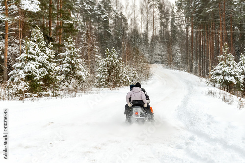 People rides on a snowmobile along the snow road in the forest.