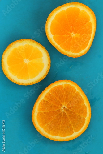 Close up of three round orange citrus slices on blue background, fresh summer mood. Stock photo blank for your design, vertical rectangular orientation.