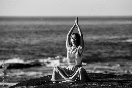A young yoga woman meditates in the lotus position sitting on rocks on the Alantic ocean coast. Black and white photo. photo