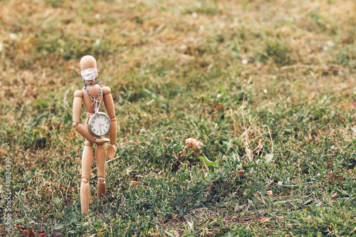 Wooden mannequin wearing medical mask with clock outdoors