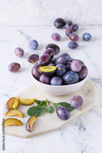 Bowl with tasty plums on light background