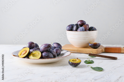 Plate with tasty plums on light background