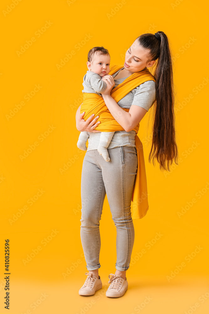 Young mother with little baby in sling on color background Young mother with little baby in sling on color background
