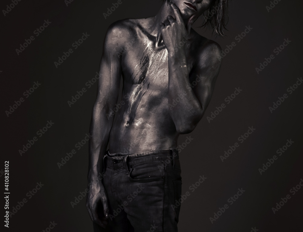 Naklejka premium Guy posing with pensive expression. Fashion and masculinity concept. Man with streams of sweat or paint on naked chest, with nude torso covered with shimmering silver.