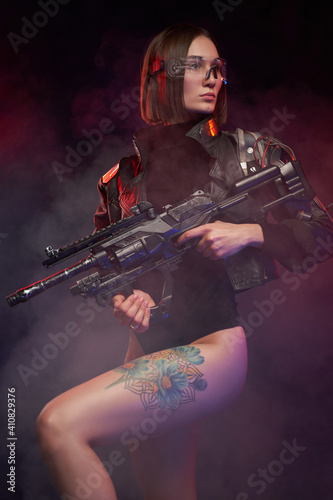 Sexual female warrior with nude and tattooed legs poses in dark and smokey background. Armed with futuristic armed beautiful woman with cybernetic implant.