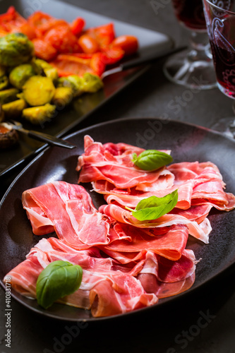 Prosciutto with different appetizers with glass of red wine on black background