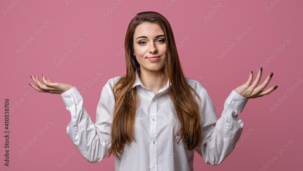 Portrait of clueless and indecisive brunette girl shrugging with hands spread sideways, pink background