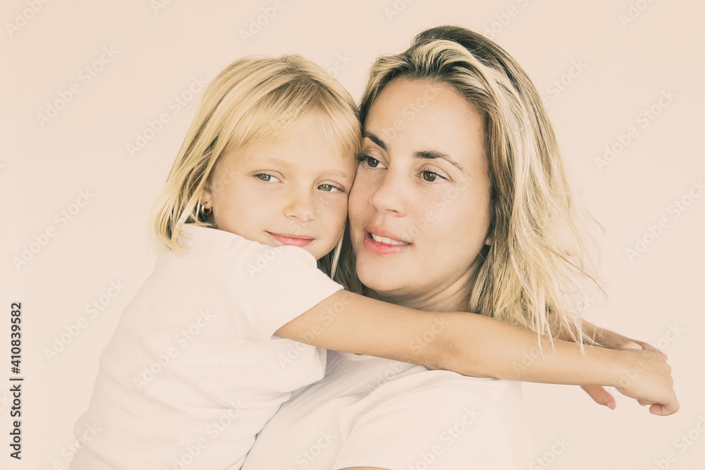 Caucasian attractive mother holding daughter and looking away. Cute little girl sitting on mom hands and embracing or hugging her on white background. Family, love and parenthood concept Caucasian attractive mother holding daughter and looking away. Cute little girl sitting on mom hands and embracing or hugging her on white background. Family, love and parenthood concept