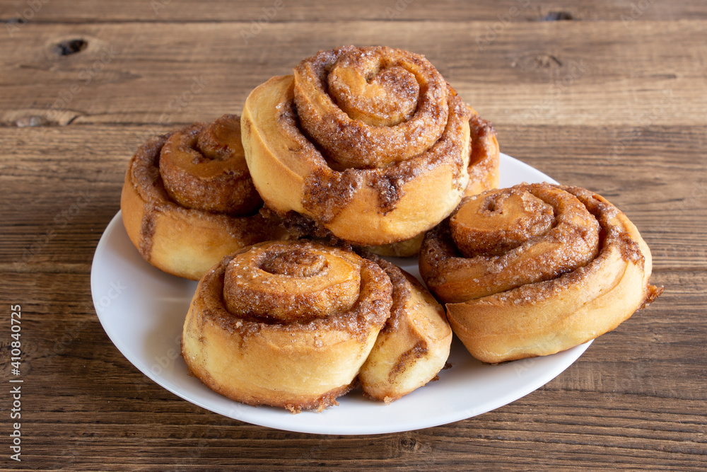 Cinnabon buns with sugar and cinnamon on a white plate on wooden background Cinnabon buns with sugar and cinnamon on a white plate on wooden background
