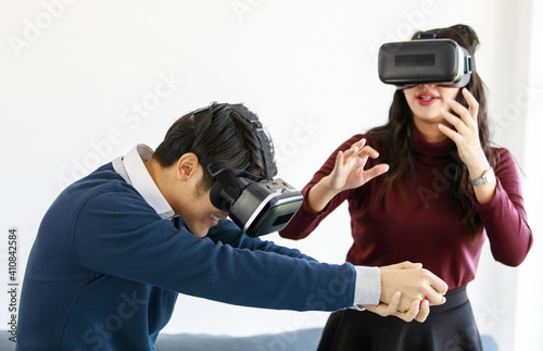 Portrait of cute smiling young Asian lover couple having fun with playing a new video game with virtual reality headset glasses together while sitting on the couch with Christmas tree background