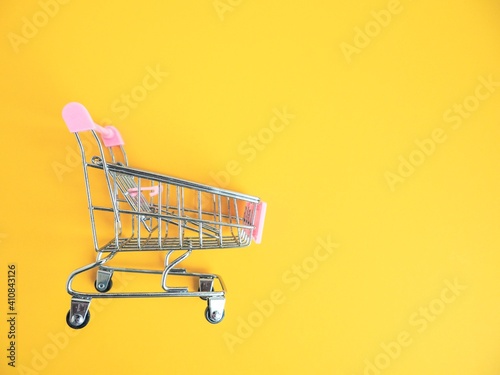 Shopping trolley on yellow background. Shopping cart in the supermarket. Sale, discount, shopaholism concept. The trend of consumer society. Top view with copy space.