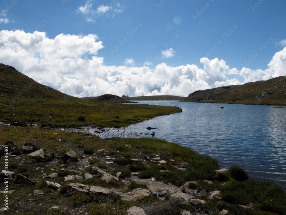 view of a small alpine lake at 2700 meters high with mountain peaks all around, on a beautiful sunny day in August