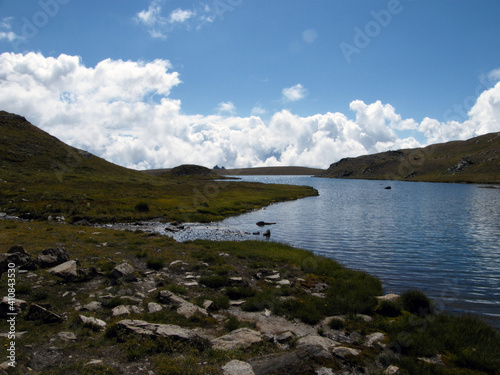 view of a small alpine lake at 2700 meters high with mountain peaks all around, on a beautiful sunny day in August