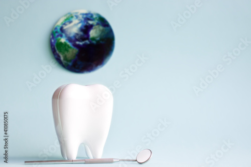 Fototapeta Naklejka Na Ścianę i Meble -  White tooth with dental mirror on blue background with planet earth in honor of international dentist day with place for text