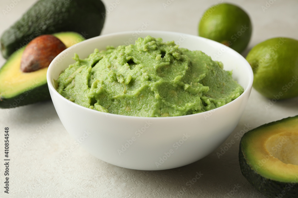 Bowl of guacamole, avocado and lime on white textured background, close up Bowl of guacamole, avocado and lime on white textured background, close up
