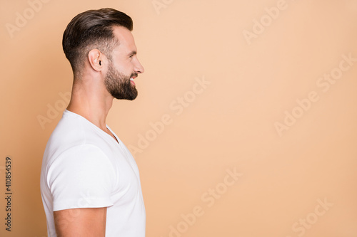 Profile side photo of young handsome man happy positive smile look empty space isolated over beige color background photo