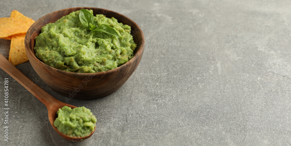 Bowl of guacamole, spoon and chips on gray background Bowl of guacamole, spoon and chips on gray background