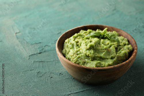 Bowl of guacamole on green textured background, space for text