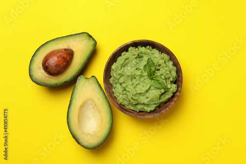 Bowl of guacamole and avocado on yellow background, top view