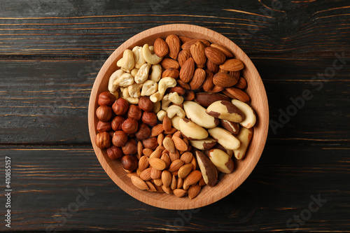 Bowl with different nuts on wooden background, top view