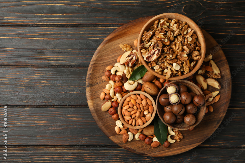 Tray with bowls with different nuts on wooden background