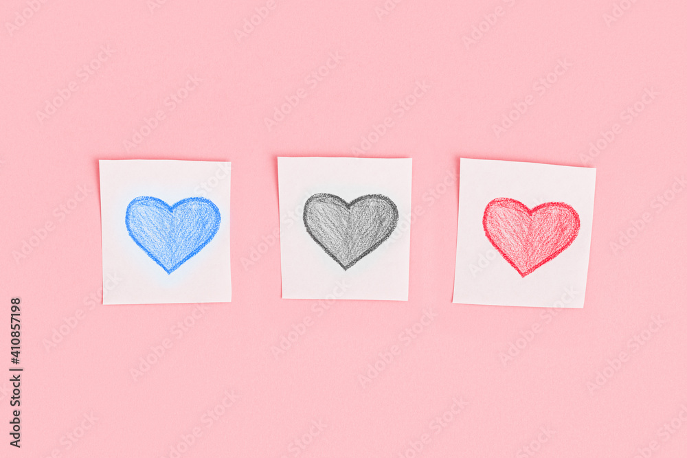 Three multicolored hearts drawn in pencil on pieces of white paper