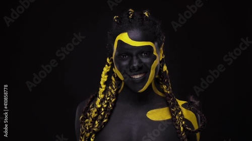 Face art. Woman with black and yellow body paint. Young african girl with colorful bodypaint. An amazing afro american model with yellow makeup. photo