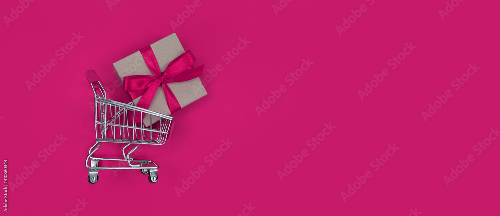 Supermarket trolley and gift box on pink background with copy space. Shopping concept.