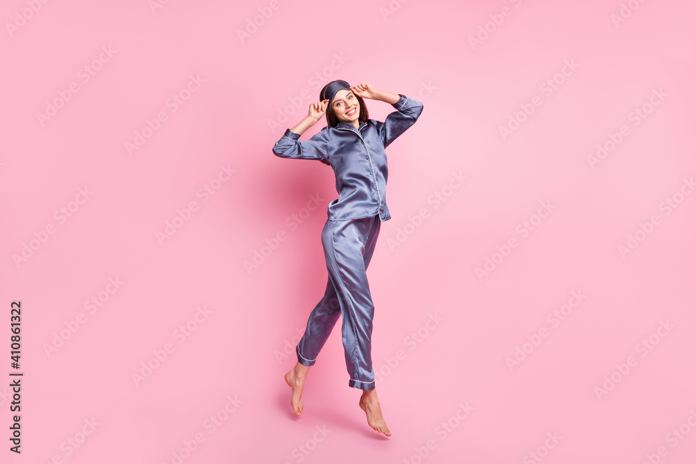 Full length body size photo of brunette in blue pajama jumping smiling touching sleeping mask isolated on pastel pink color background - obrazy, fototapety, plakaty 