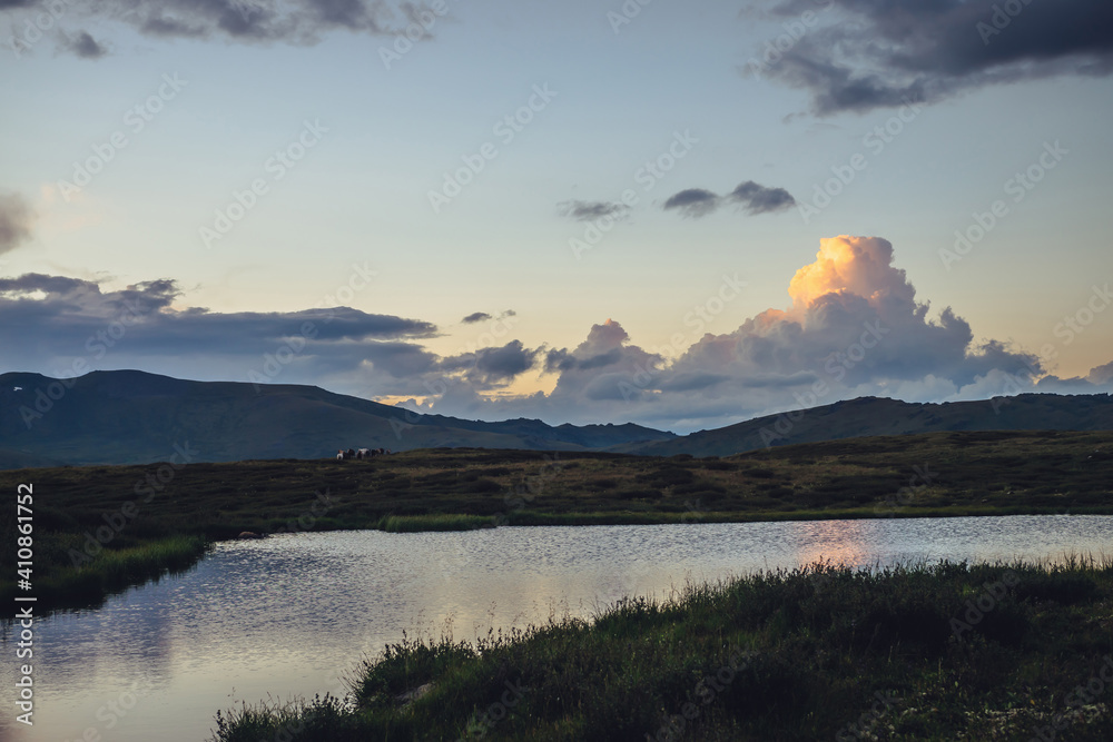 Scenic sunset landscape with yellow big cloud in form of explosion above mountain lake. Awesome giant cloud reflected in lake water in sunrise. Huge cloud of illuminating color in dawn gradient sky.