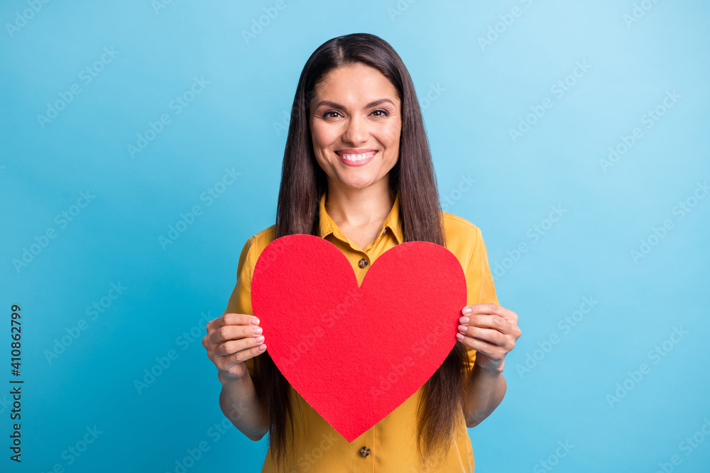 Portrait of pretty cheerful lady arms hold paper heart postcard toothy smile isolated on blue color background Portrait of pretty cheerful lady arms hold paper heart postcard toothy smile isolated on blue color background