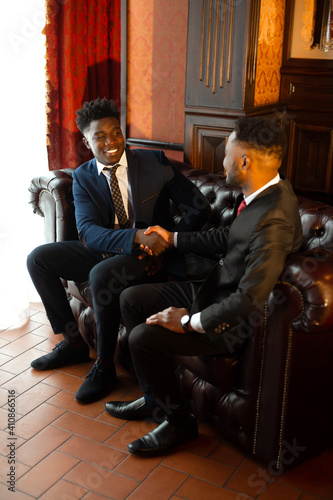 two handsome african men in suits shaking hands indoors 