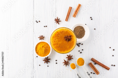 Foto Golden turmeric latte in glass, spices and cinnamon on white wooden background