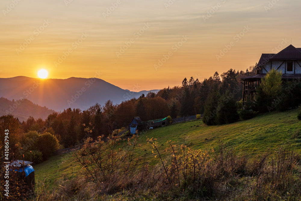 Fantastic sunset in a small mountain village. Panoramic view. Delicate clouds against the orange sky. Colorful autumn in the Ukrainian Carpathians. Beautiful nature scene.