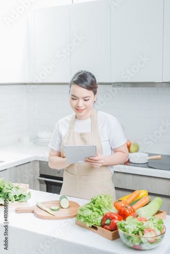 beautiful korean woman in apron holding tablet pad looking at list and checking fresh vegetables